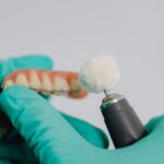 dentist wearing gloves polishes a dental prosthetic using a specialized tool in a clinical setting