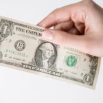 close up of a caucasian hand holding a us one dollar bill against a white background